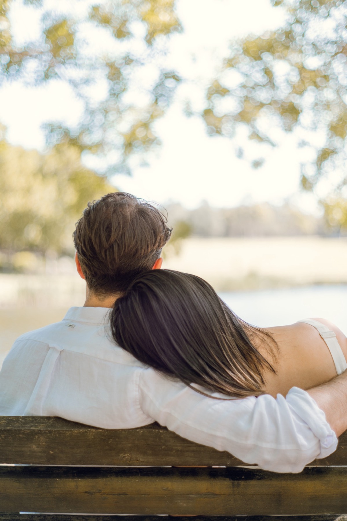 Damon and Christina seen from behind on a park bench by a lake