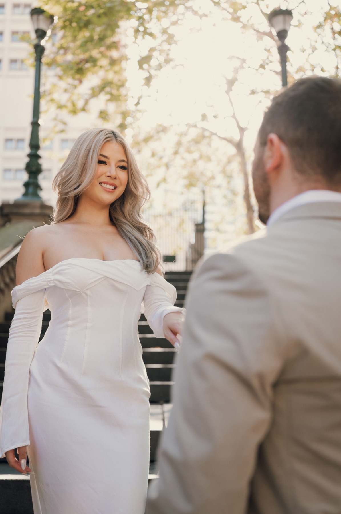 Kim in an off-the-shoulder white dress smiling at Dave on the stairs