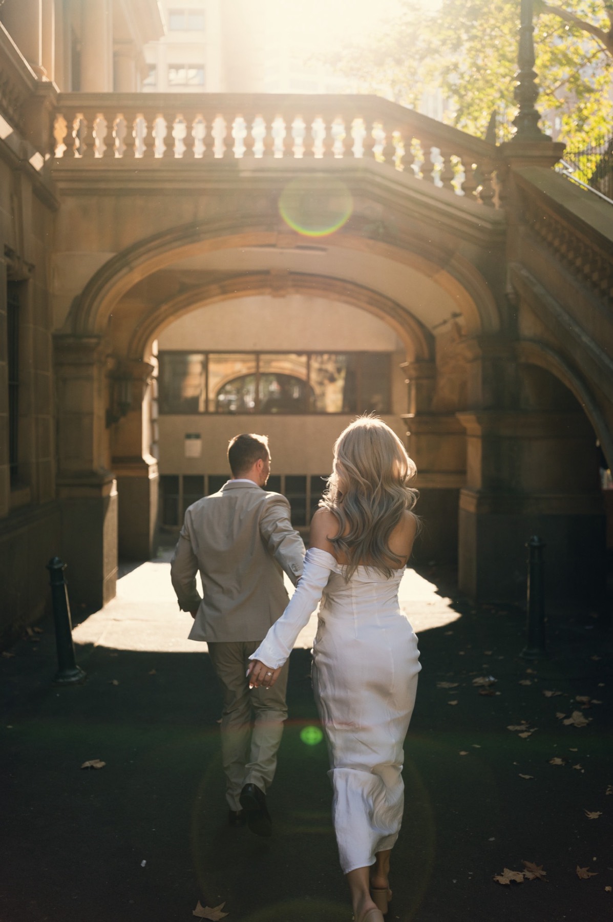 The couple walking away through a sandstone archway into golden afternoon light