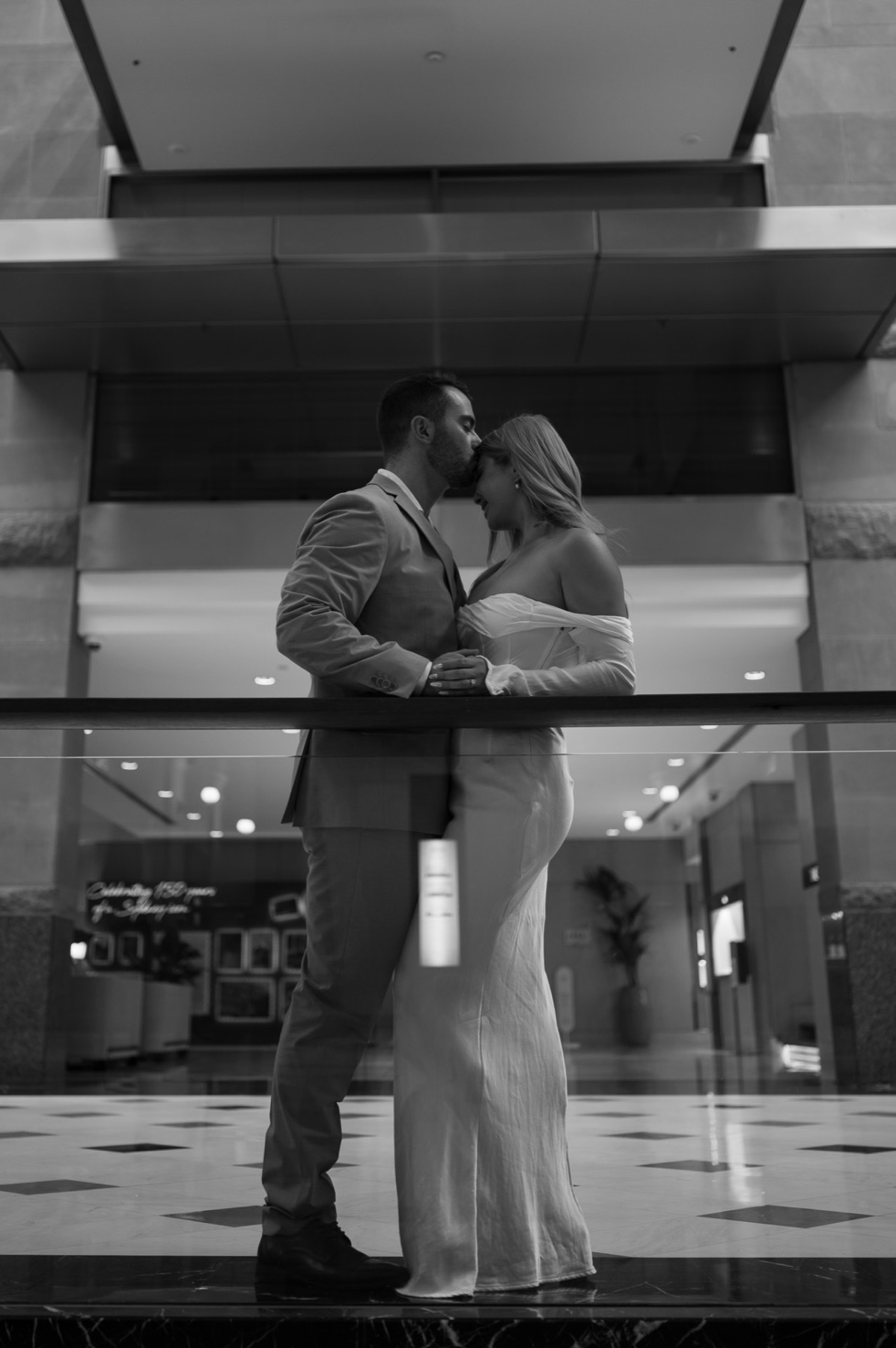 Black and white reflection of the couple kissing in a glass-walled lobby