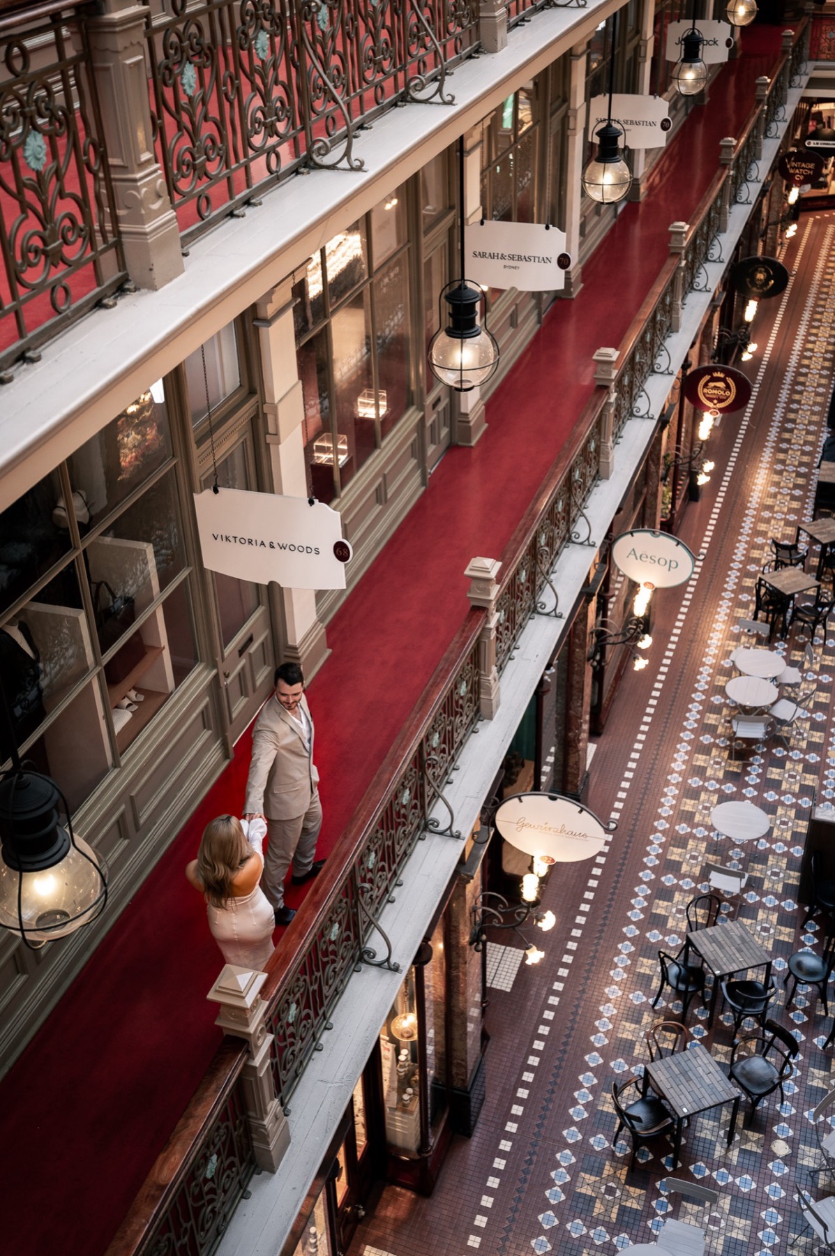 Looking down on Kim and Dave at a balcony railing above a red-carpeted arcade walkway