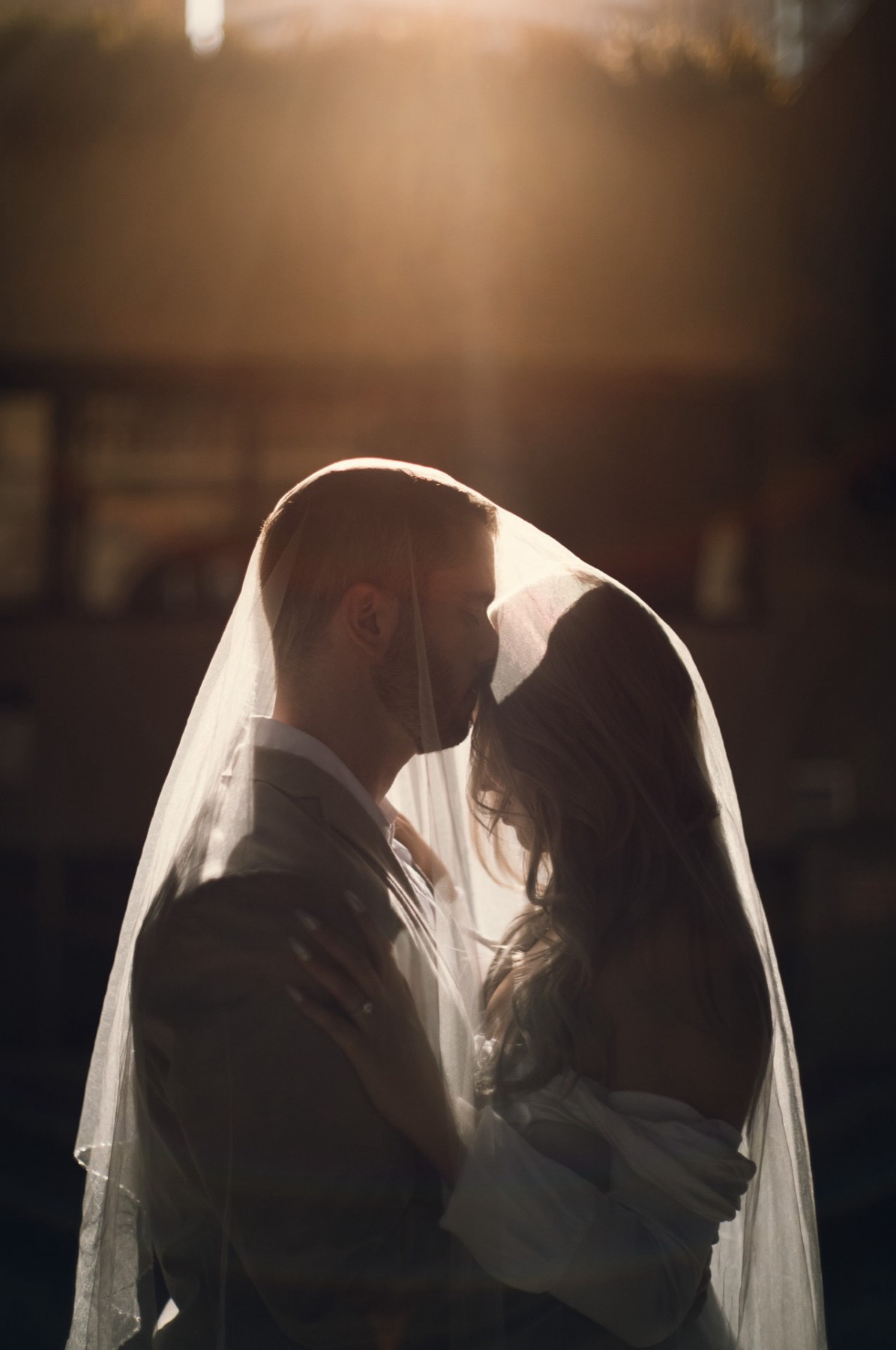 The couple kissing beneath Kim's veil, backlit so the veil glows